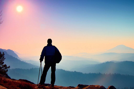旅游与剪影手杆。与运动背包徒步旅行者站在岩石看法点以上迷雾笼罩的山谷。阳光明媚的早晨，在洛基山脉