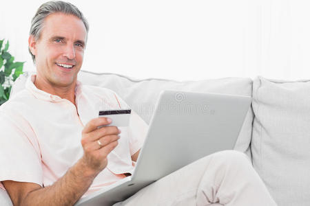 坐在沙发上用笔记本电脑上网购物的快乐男人