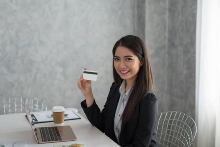 美丽的亚洲年轻女商人在她的工作站上持有银行卡。商业金融银行概念