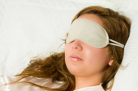 布鲁内特舒适地将头靠在白色的枕头上，蒙上眼睛睡觉盖的眼睛