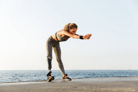 全长的重点残疾运动员妇女与假肢做伸展运动, 而站在海滩