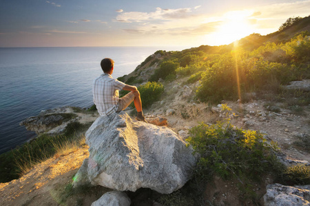 男人坐在山上的岩石上看日出