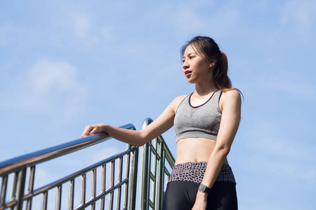 年轻女子在公园的栅栏上慢跑运动后放松, 以清新她的身体和享受温暖的光线在早晨。年轻的亚洲妇女休息 execise 跑步。户外运动