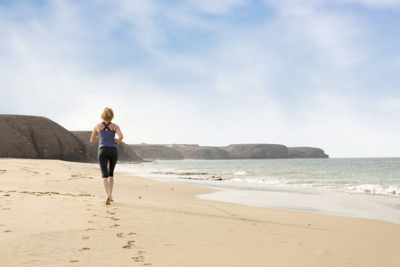 在留下足迹的沙滩上赤脚跑步的女人