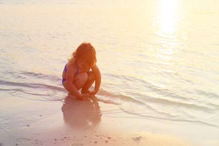 小女孩在日落海滩上玩沙子