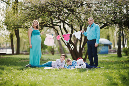 幸福的怀孕夫妇与两个儿子拿着女童婴儿衣服