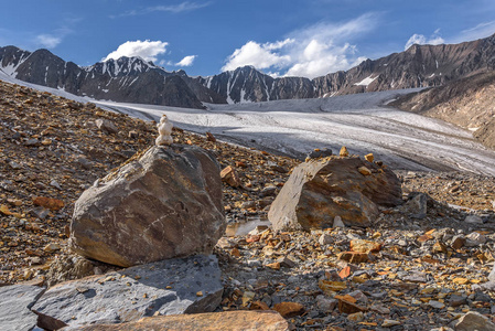 山上一座石头上的小雪人, 在夏季的冰川山峰和蓝天的背景下