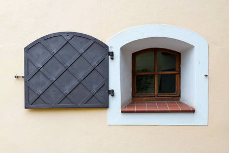 在中世纪的房子的黄色墙上的一个小窗口被一个铁快门保护。历史欧洲城市细节概念