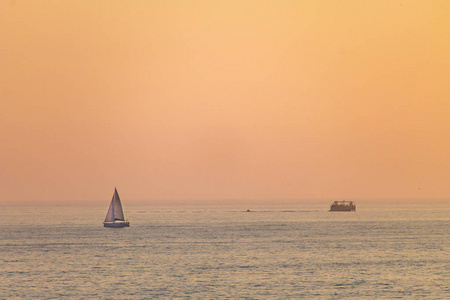 一艘遥远的帆船在日落时沿着海面航行, 背景是橙色的天空。