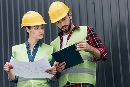 hardhats 的成人建筑师在屋顶上使用蓝图和剪贴板