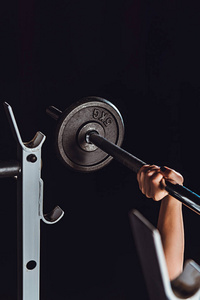 女性健美运动员锻炼与杠铃在健身房, 黑色背景的裁剪图像