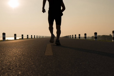 人亚洲腿的下来看法在时间奔跑在日出期间在水坝路锻炼。健康的生活方式