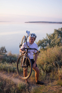 自行车车手独自骑在岩石路, 湖和森林背景在美丽的日落
