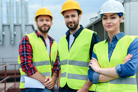 专业工程师在安全背心和 hardhats 摆姿势与交叉武器