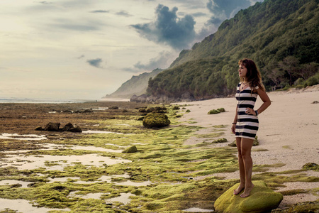 孤独的女孩站在岩石海滩和期待着大海