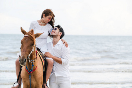 年轻夫妇去蜜月骑马在海滩上的夏天假期