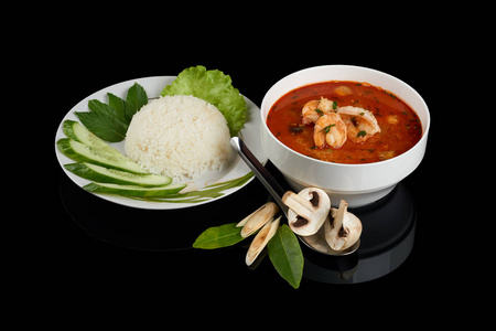 汤姆和汤是一种酸辣的泰国汤, 通常用虾煮。配有米饭蔬菜和筷子。在黑色反射背景下隔离