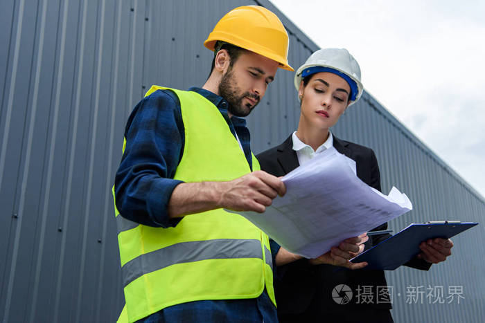 戴头盔的女工程师和男工人的建筑图纸