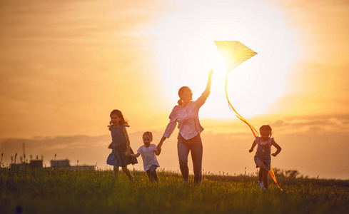 快乐的家庭在户外玩耍。母亲和孩子们跑在草地上, 在夏天的自然风筝