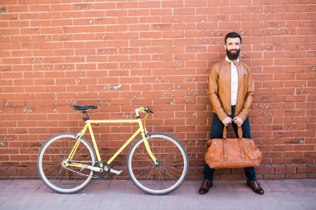 年轻时尚的男人，留着胡子砖背景站附近自行车与手中的包