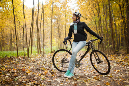 女孩的图片在头盔, 牛仔裤旁边的自行车在秋季公园