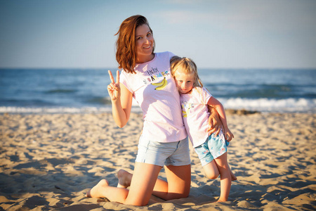 年轻母亲与女儿在海滩在海背景在日落