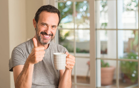 中年男子喝咖啡在一杯快乐的大微笑做 ok 标志, 拇指与手指, 优秀的标志