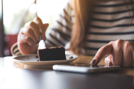 特写图像的女人使用, 触摸和指向 atsmart 手机, 而在咖啡馆吃布朗尼蛋糕
