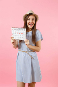 在蓝色礼服的年轻妇女的画像, 帽子举行期间检查月经日的日历在明亮的趋向粉红色背景被隔绝。医疗保健妇科概念复制空间