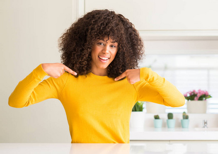 在厨房穿着黄色毛衣的非洲裔美国妇女脸上带着微笑, 用手指自豪和快乐地指着自己。