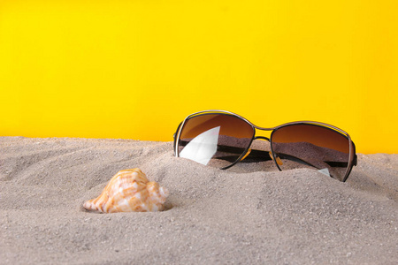 眼镜从太阳与贝壳在海的沙子在明亮的黄色纸背景