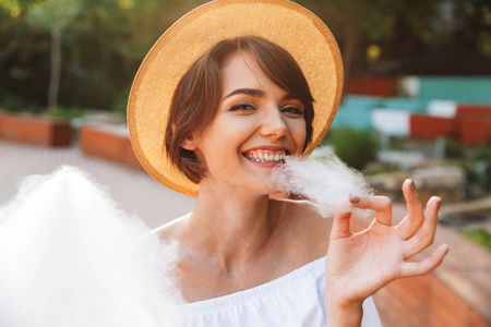 在公园里穿着夏天衣服的微笑的年轻女孩的特写吃棉花糖