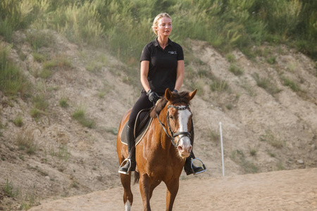户外拍摄的美女金发女郎白天骑马。穿着运动服装的年轻女子在马场享受骑马