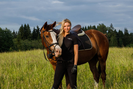 户外拍摄的美女金发女郎白天骑马。穿着运动服装的年轻女子在马场享受骑马