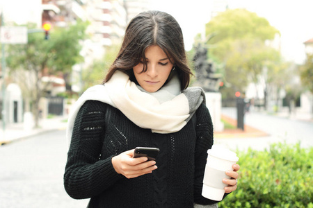 美丽的年轻妇女发送信息与智能手机在街上