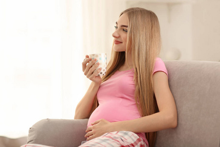 在家沙发上喝茶的年轻孕妇