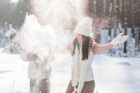 年轻漂亮的母亲和她的小女孩在户外在冬天的乐趣。开朗的孩子和她美丽的妈妈玩雪的性质。吹雪
