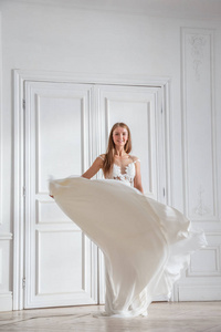 时装拍摄的美丽的金发女子白色礼服站在白色的内部背景