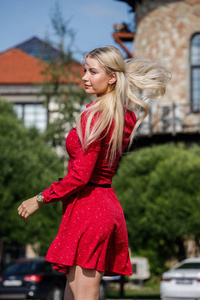 户外时装肖像美丽的金发女郎穿着红色礼服站在城市街道上白天