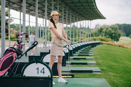 女高尔夫球运动员在马球和帽子与高尔夫球俱乐部的目光远离高尔夫球场