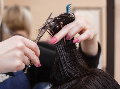 理发师对理发与热剪刀片头发一个年轻的女孩，一个在一家美容院的黑发