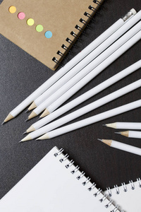 白色的弹簧垫和简单的铅笔, 用于笔记和草图。在一个不同颜色的笔记本附近。学校和教学文具。在黑暗背景下