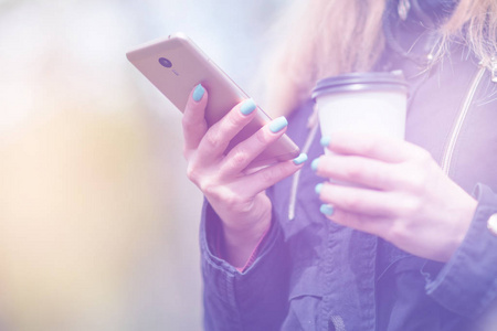 一个女孩早上在公园里走着智能手机和咖啡, 光色调