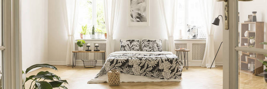 全景的简约, 宽敞的卧室内饰与米色装饰, 木制家具和舒适的双人床上的人字形实木复合地板