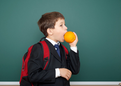 小男孩穿着黑色西装吃橙色的绿色黑板背