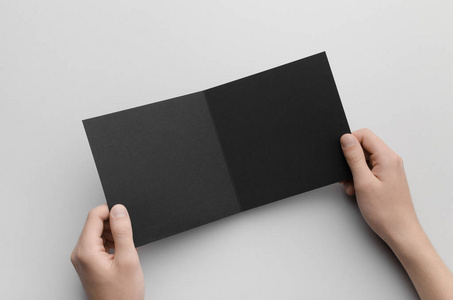 黑色正方形双折叠小册子模型男性手拿着黑色双折在灰色背景上