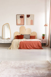 在床上的红色床单在现代卧室内部与海报和镜子在内阁。真实照片