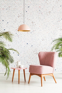 粉红色的灯以上桌子和扶手椅在花纹客厅内部与植物。真实照片