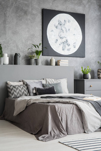 现代居室的垂直景观, 灰色的色彩与一个大床, 在前面的枕头和床上用品, 墙上的月亮画。真实照片