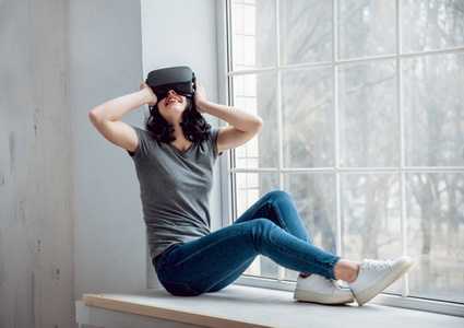 穿着虚拟现实护目镜的年轻女孩坐在窗边